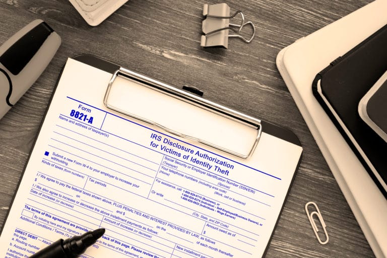 IRS identity theft form on clipboard, desk items nearby.